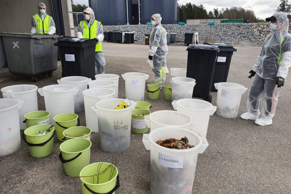 Saaveja ja ämpäreitä, joihin on lajiteltu jätteitä sekä tutkimusryhmän jäseniä suojapuvuissa