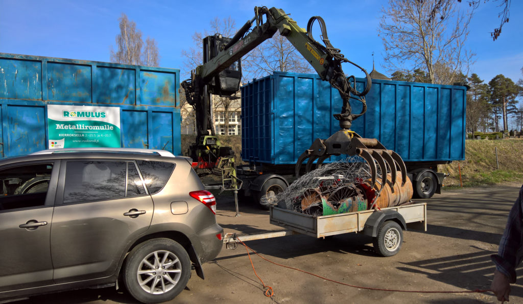 Metallinkeräysauto Romulus kahmaisee kourallaan peräkärrystä metallijätteitä